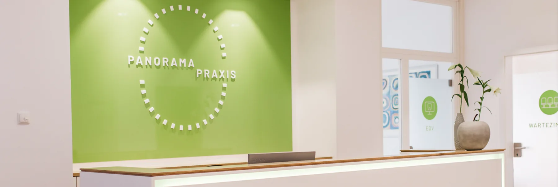 Der Empfang der Panorama Praxis vor der grünen Wand mit dem Praxislogo