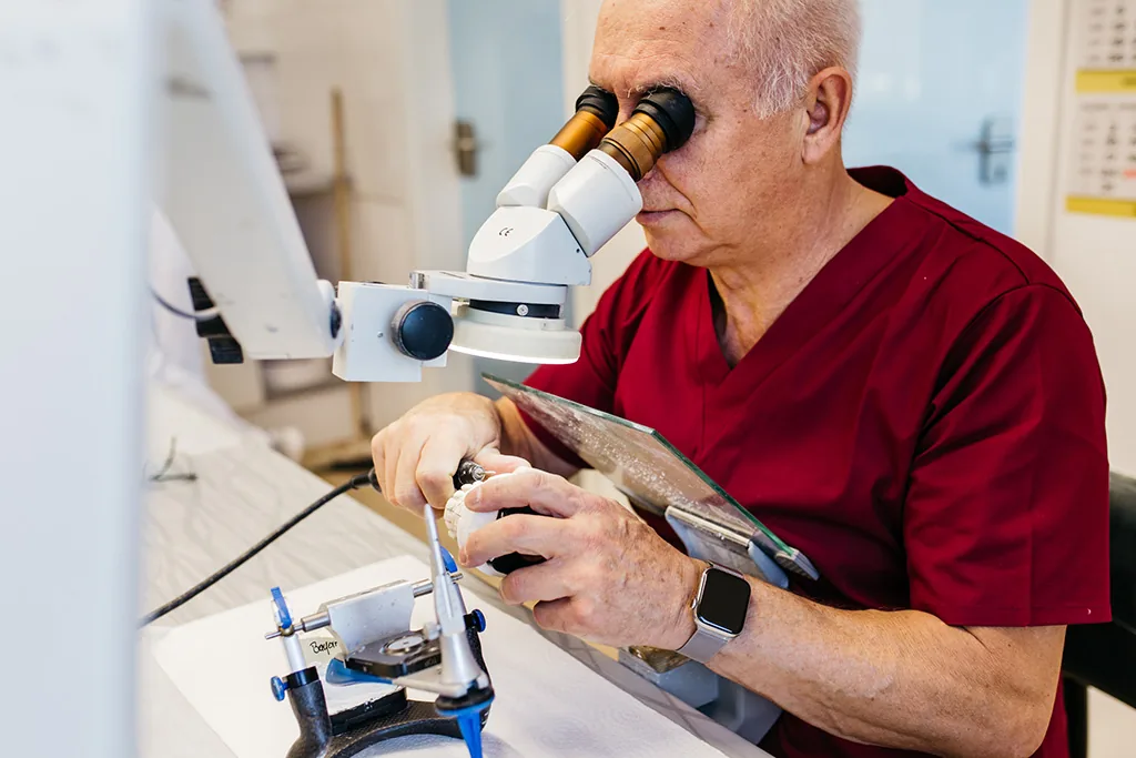 Zahntechniker prüft eine Arbeit unter dem Stereomikroskop