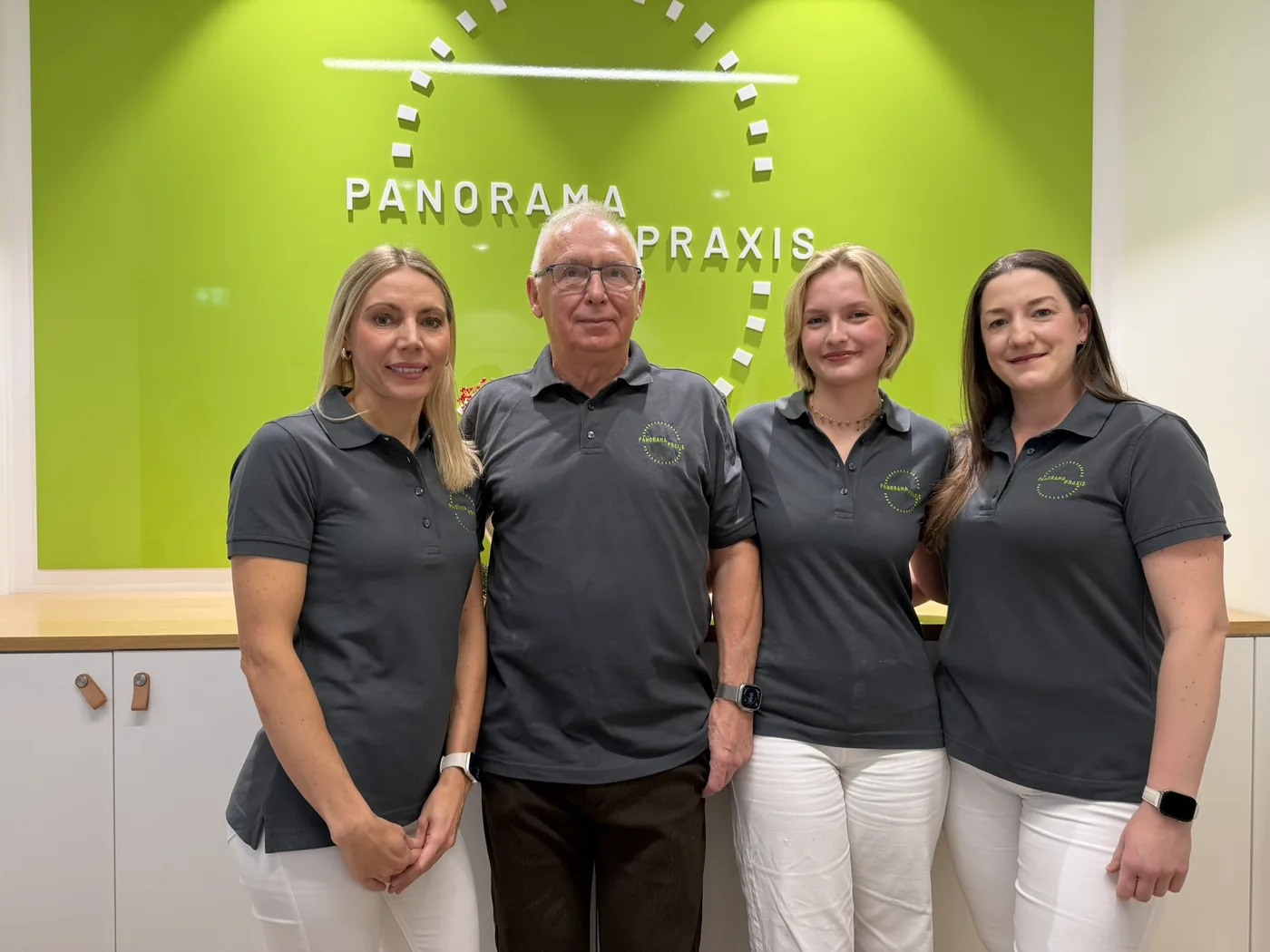 Das Team der Panorama Praxis am Empfang vor der grünen Logowand